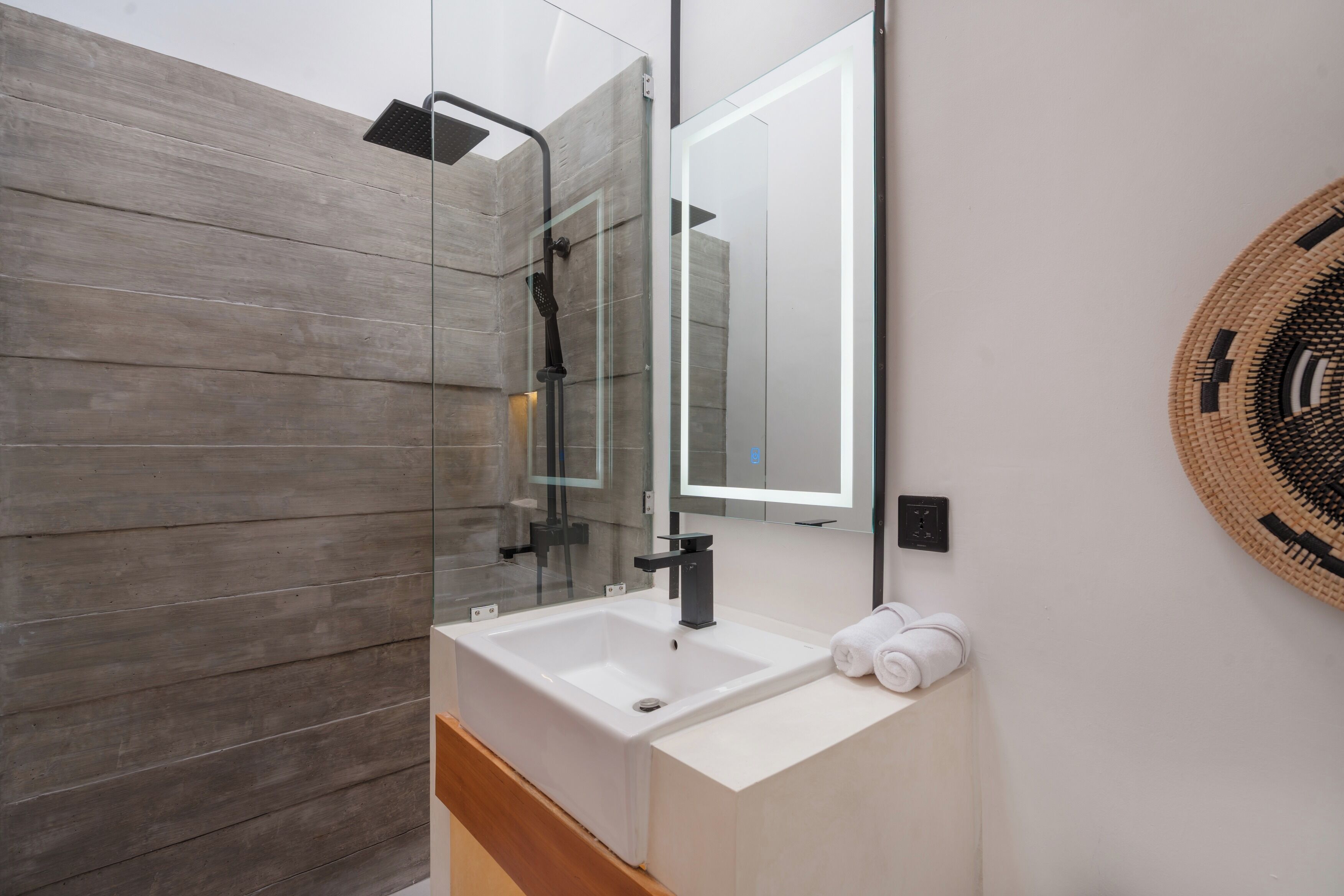 Un baño moderno con ducha envuelta en vidrio, un lavamanos blanco y un espejo grande.