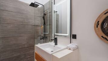 Un baño moderno con ducha envuelta en vidrio, un lavamanos blanco y un espejo grande.