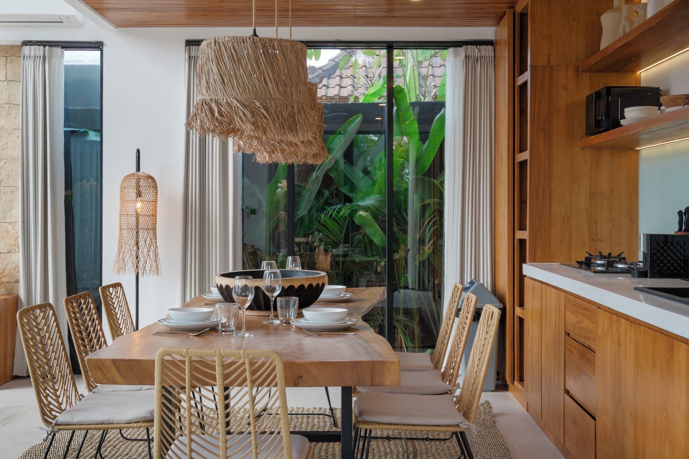 A dining area with a wooden table, wicker chairs, and a hanging light fixture.