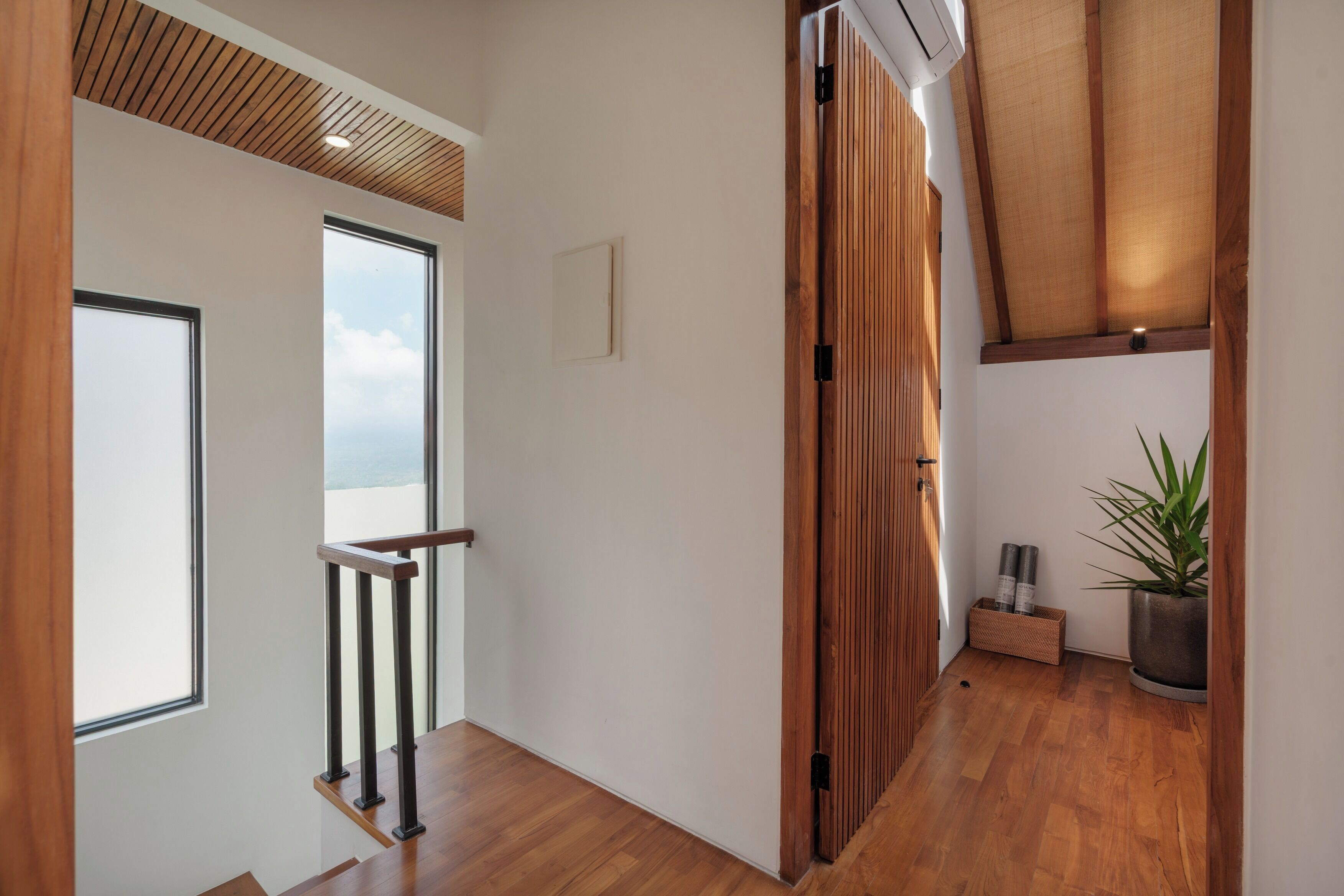A hallway with wooden flooring, a view through a glass door, a ceiling with wooden slats, and a potted plant.