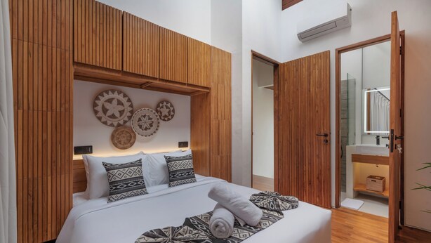 Un dormitorio moderno con cabecera de madera, cama grande con almohadones estampados y un muro decorado con adornos circulares.