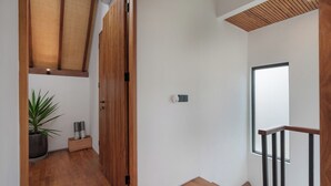 Un pasillo con suelo de madera, una planta en maceta, una cesta con colchonetas de yoga y una puerta de madera.