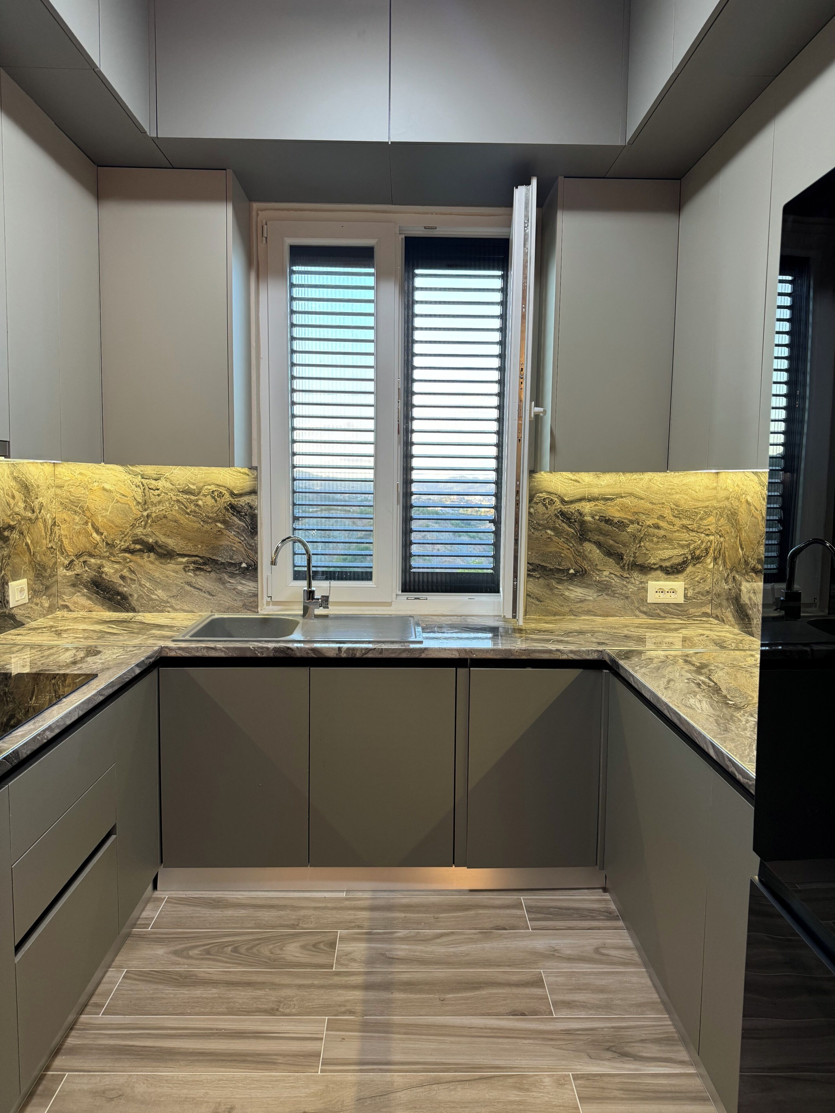 Una cocina moderna con un lavamanos integrado, dos ventanas con persianas y una encimera de mármol.
