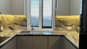 Una cocina moderna con un lavamanos integrado, dos ventanas con persianas y una encimera de mármol.