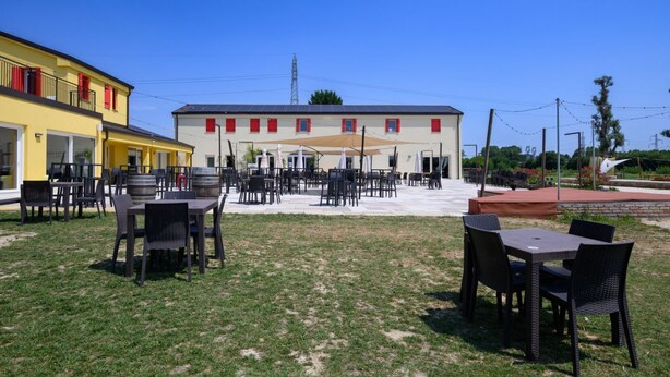 Ein Außenbereich mit Tischen und Stühlen, eine überdachte Terrasse und ein Gebäude mit roten Fensterrahmen.