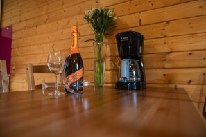 Een houten tafel met een fles wijn, een glas en een koffiezetapparaat.