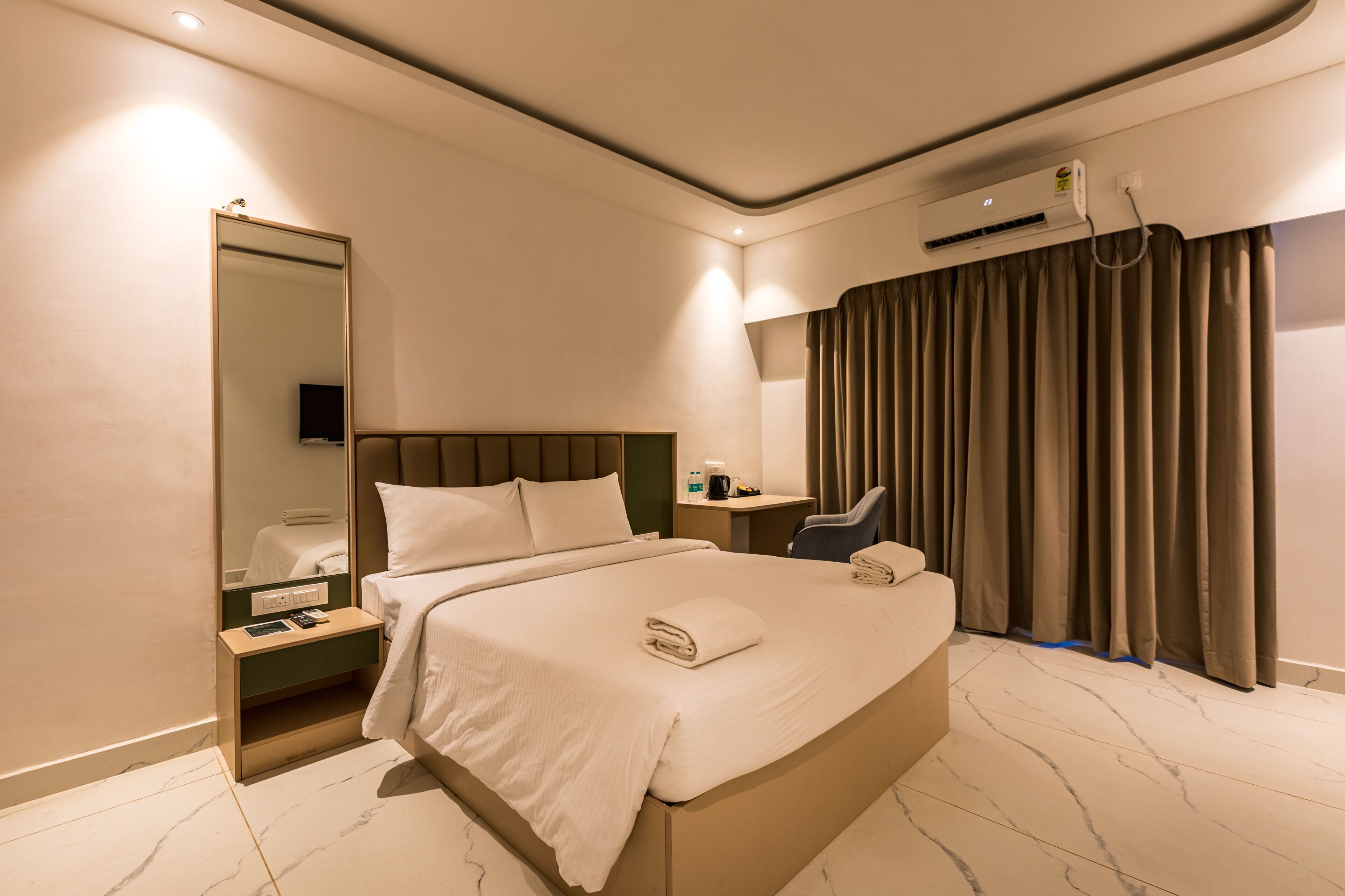 Habitació d'hotel amb un llit gran, una taula de nit, un mirall, un escriptori i una finestra amb cortines.