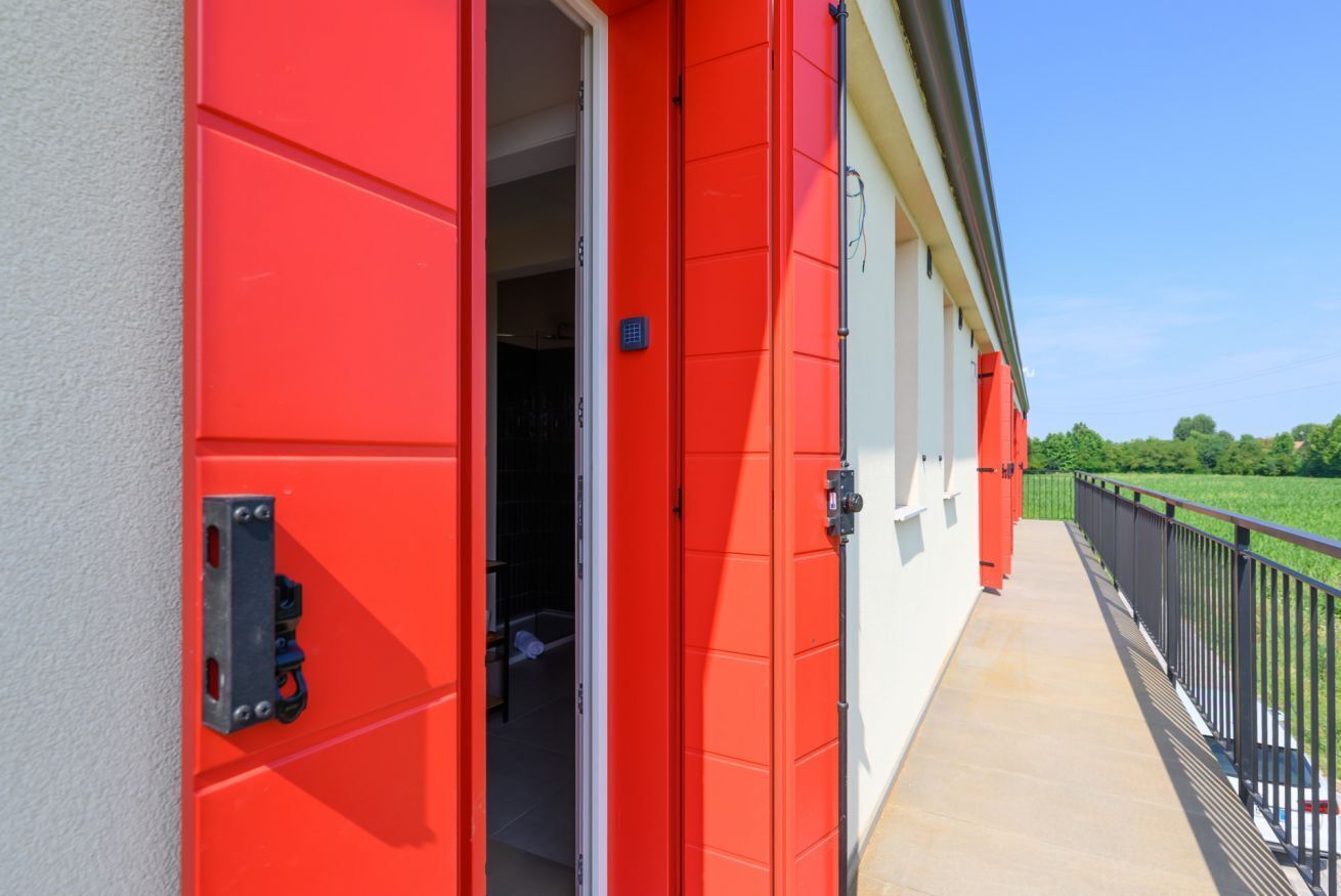 Un edificio rojo con una puerta abierta que da a un cuarto con cama y ventana.