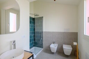 Ein Badezimmer mit einer Duschkabine, einem weißen Waschbecken, einem Bidet und einer Toilette.