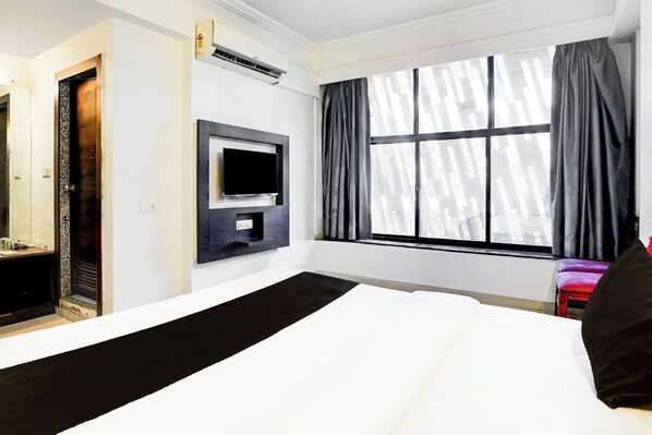 A hotel room with a large bed, a flat-screen TV mounted on the wall, and a window with curtains.