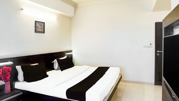 Una habitación de hotel con una cama, una mesita de noche, un florero con flores, un cuadro en la pared y un televisor.