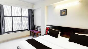 Une chambre d’hôtel avec un grand lit, une chaise, un bureau et une fenêtre avec des rideaux.
