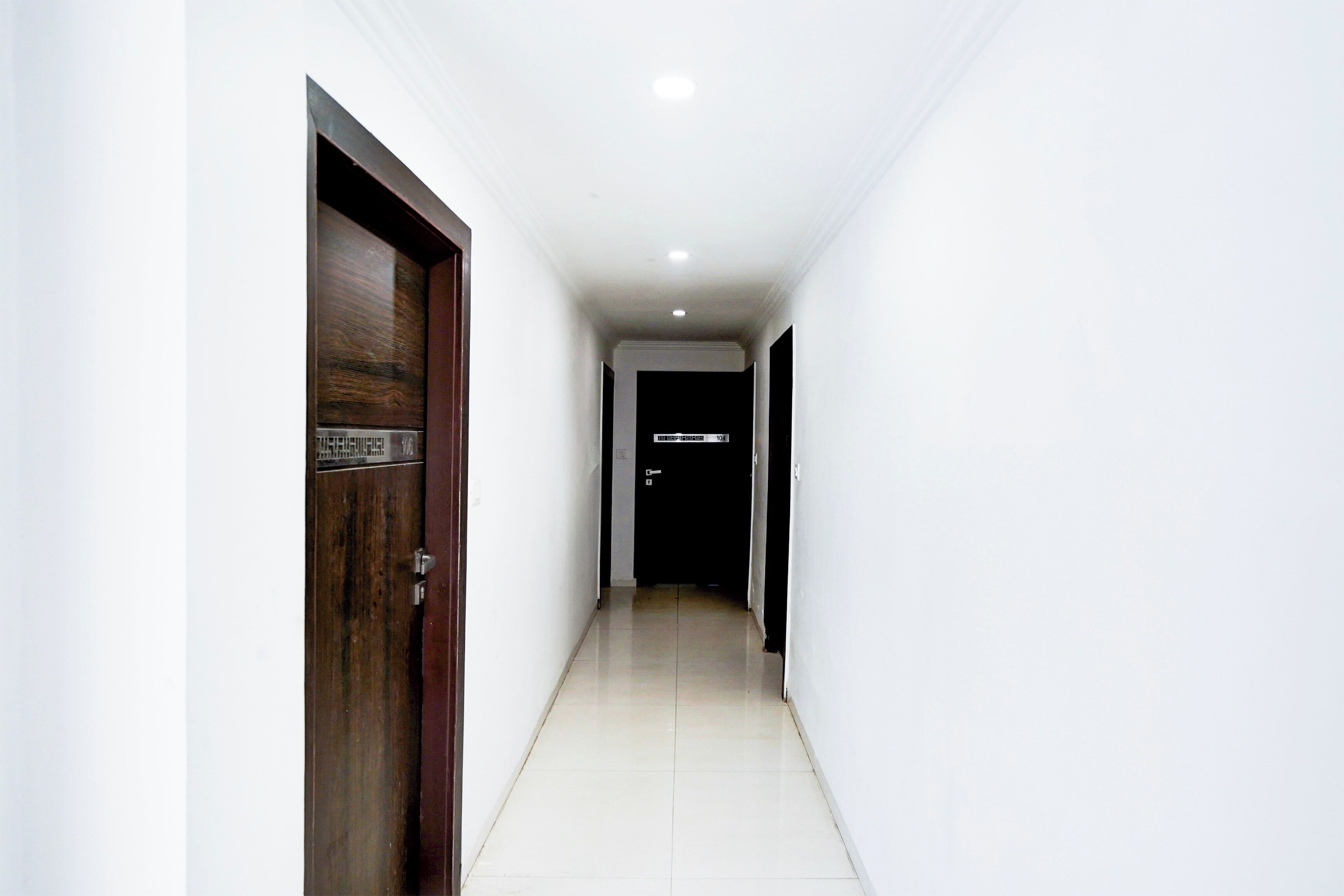 Um corredor com uma porta de madeira à esquerda e uma porta preta no final.