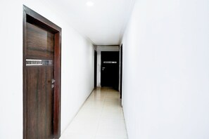 A hallway with a wooden door on the left and a black door with a sign on the right. - Super Collection O Maninagar (Ahmedabad)
