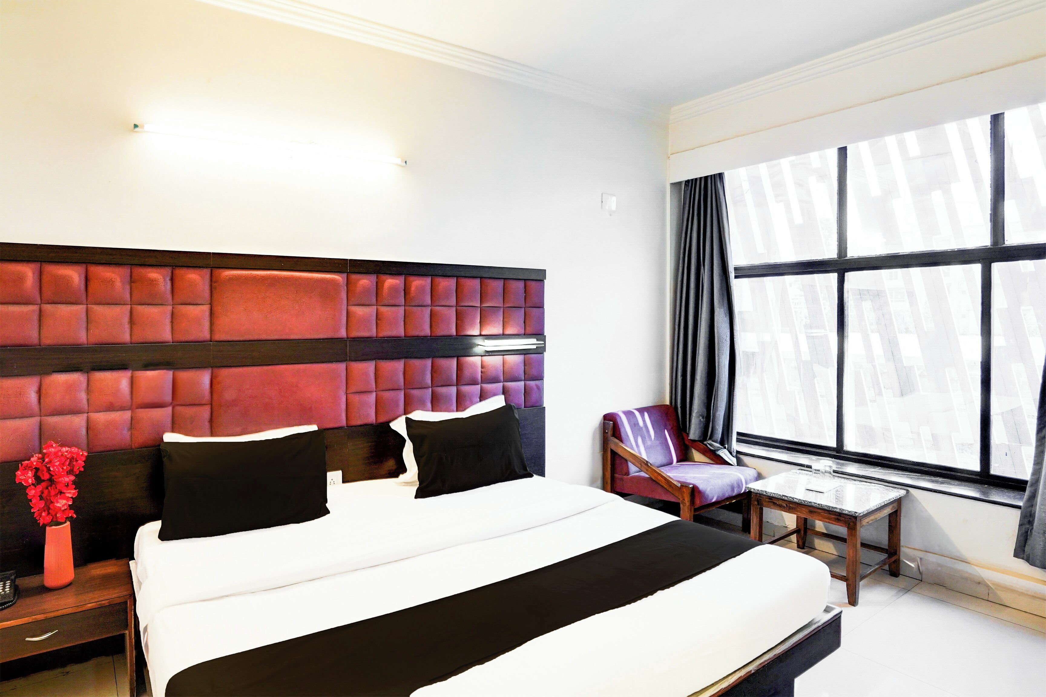 Een hotelkamer met een groot bed, een nachtkastje, een stoel en een raam met gordijnen.