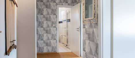 A hallway with patterned walls, a door with a mirror, and a radiator.