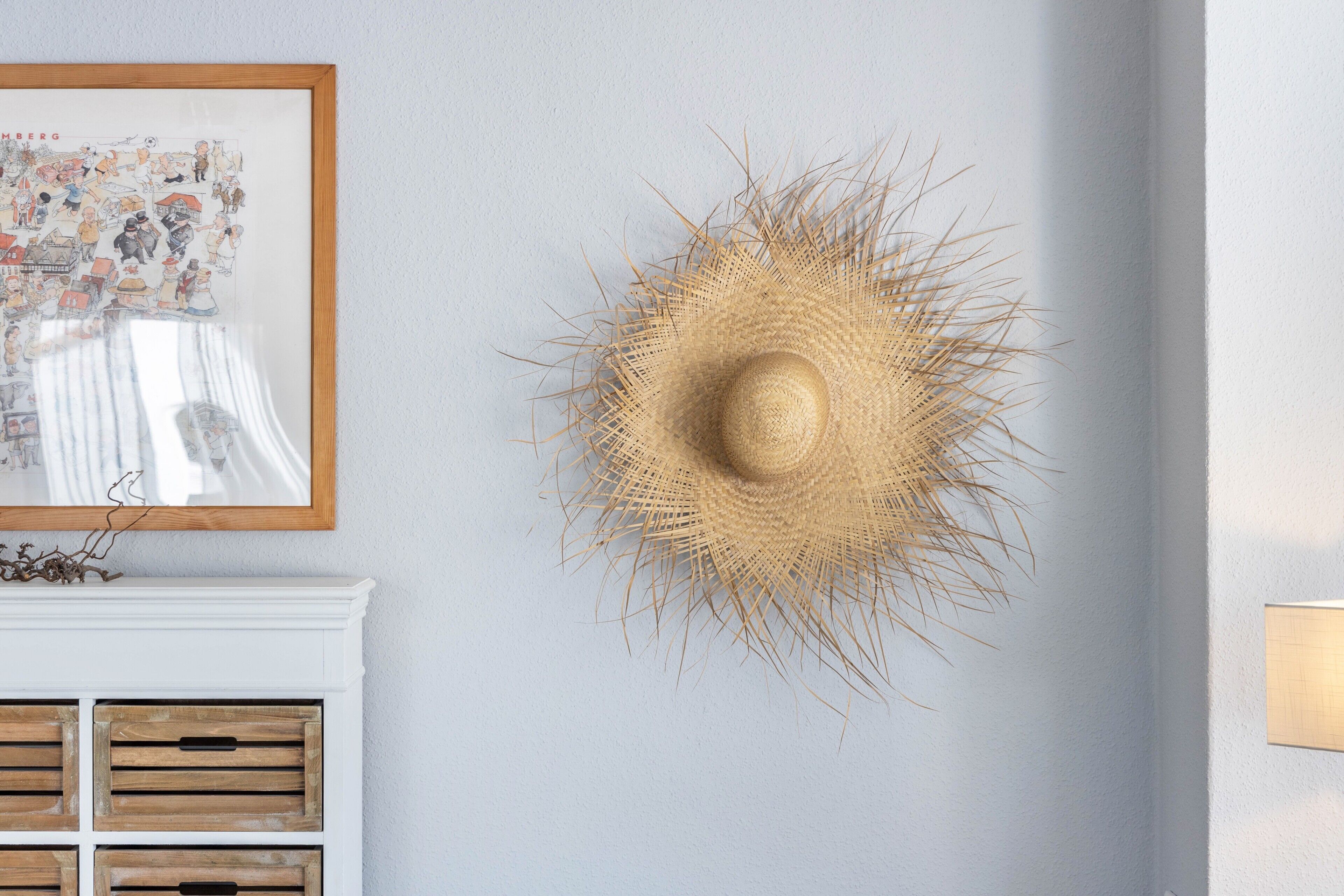 Una stanza con un cappello tessuto appeso al muro, una mappa incorniciata e un caminetto bianco con persiane in legno.