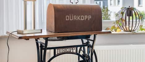 A wooden chest with 'DURKOPP' engraved on it, placed on a table with a lamp beside it.