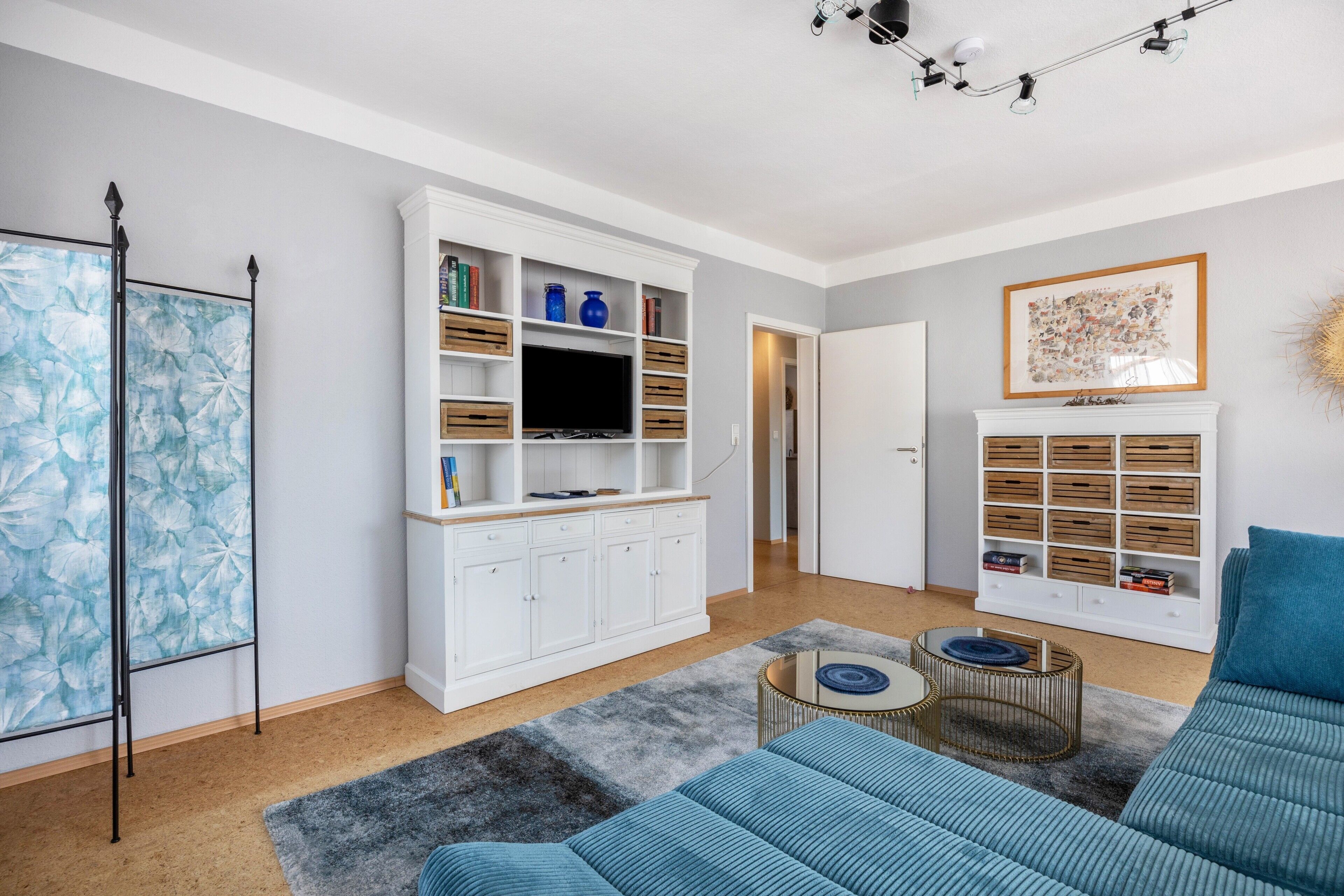 A modern living room with a white entertainment unit, a blue sofa, and a grey rug.