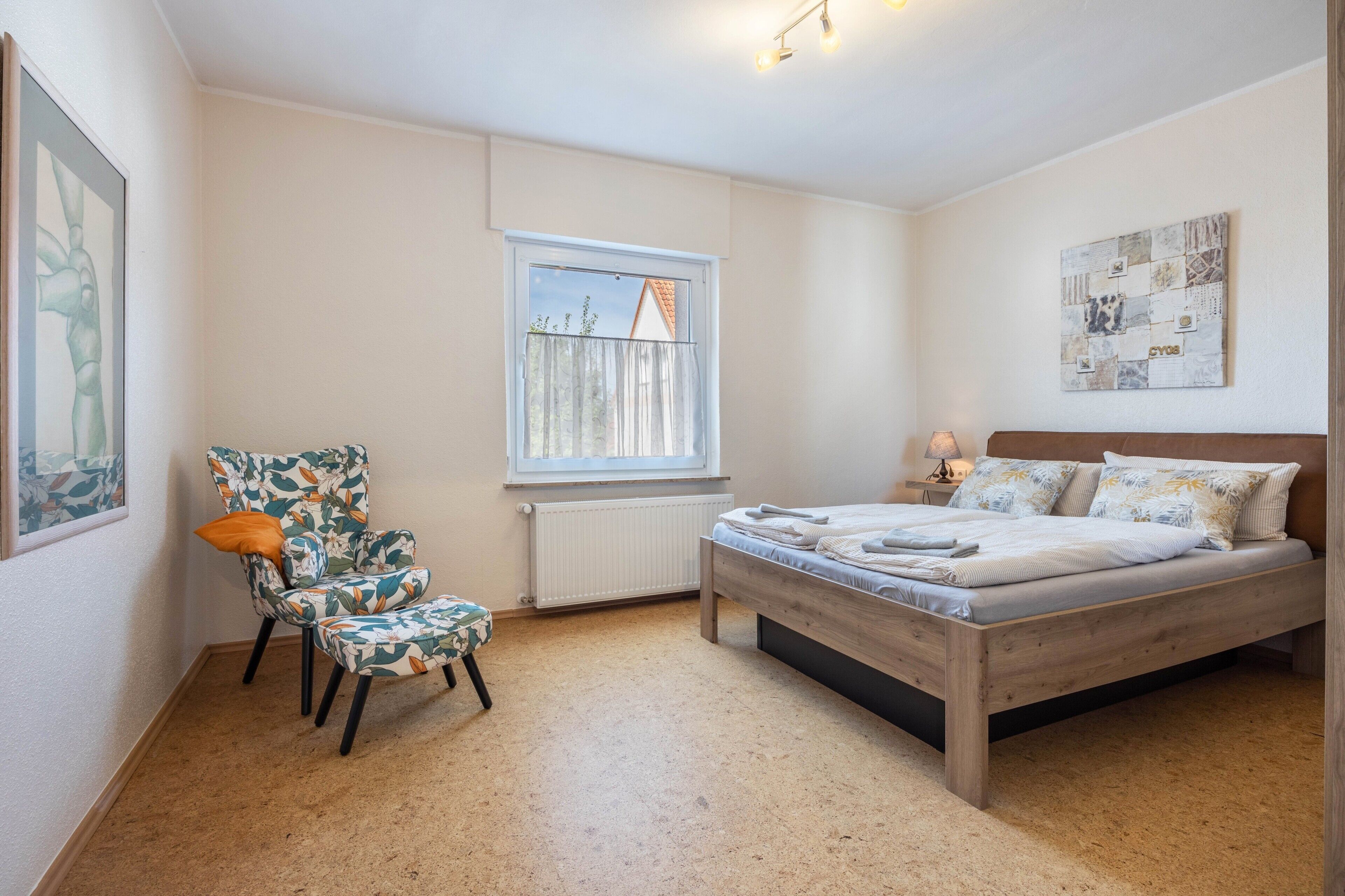 Ein Schlafzimmer mit einem Bett, einem Sessel, einem Fenster und einer Wand mit Kunstwerken.