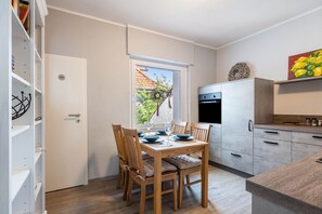 Eine kompakte Küche mit Essbereich, einem eingebauten Backofen und Blick auf einen Garten durch ein Fenster.