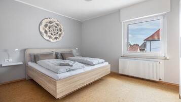 A bedroom with a bed, a wall-mounted decorative plate, a window with a view of buildings, and a radiator.