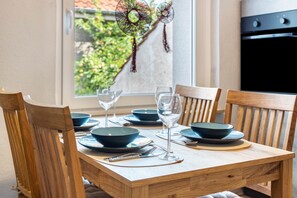 Una mesa de comedor con platos, fuentes, cubiertos y copas de vino, rodeada de sillas.