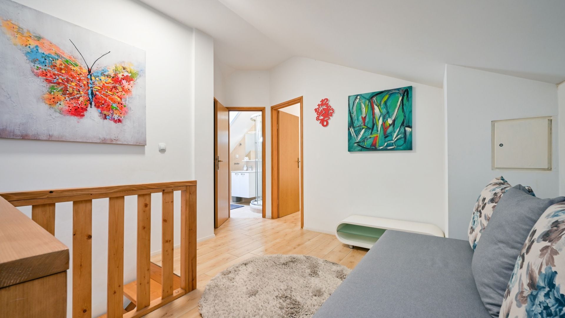 A room with a wooden staircase, a bed with floral bedding, and two abstract paintings on the walls.