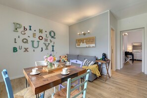 A dining area with a wooden table set for four, a grey sofa, and a wall with alphabet letters. - Santo Spirito – Part of a villa with a pool (Toscana)