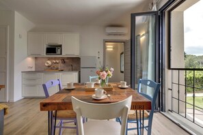 Een eethoek met een houten tafel, witte stoelen en uitzicht op de omgeving door een glazen deur.