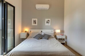 Een slaapkamer met een bed, twee nachtkastjes, een wandairconditioner en twee ingelijste foto's.