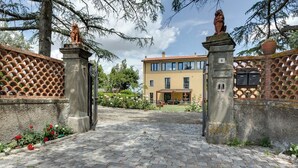 En asfalteret indgang med en port, en bygning med gul facade, og en statue øverst på porten.