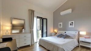Et soveværelse med seng, to sengeborde, kommode, spejl og en aircondition.