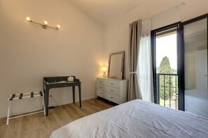 Ein Schlafzimmer mit einem Bett, einem Schreibtisch, einer Kommode, einem Spiegel und einem Fenster mit Vorhängen.