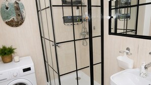 Ett badrum med en dusch som är avskärmad med glasväggar, en tvättmaskin, ett handfat och en dekorativ väggdekoration.