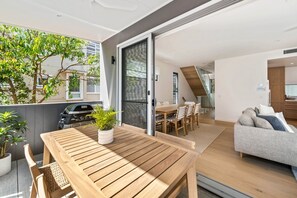 A modern apartment with a wooden dining table, a sofa, and a staircase leading to an upper floor.