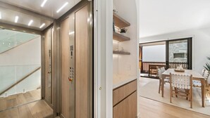 Een modern interieur met een houten trap, een eetgedeelte met een tafel en stoelen, en uitzicht op het buiten via een glazen deur.