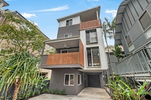A modern multi-story residential building with a flat roof, large windows, and a balcony with wooden railings. - Luxury Retreat - Villa 17 on Hastings St (Noosa Heads)