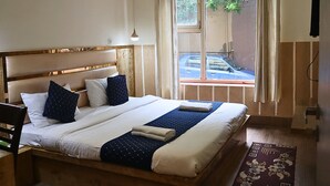 Ein Hotelzimmer mit Bett, einem Vorhangfenster, einer Wand-Klimaanlage und Blick auf ein geparktes Auto vor dem Haus.