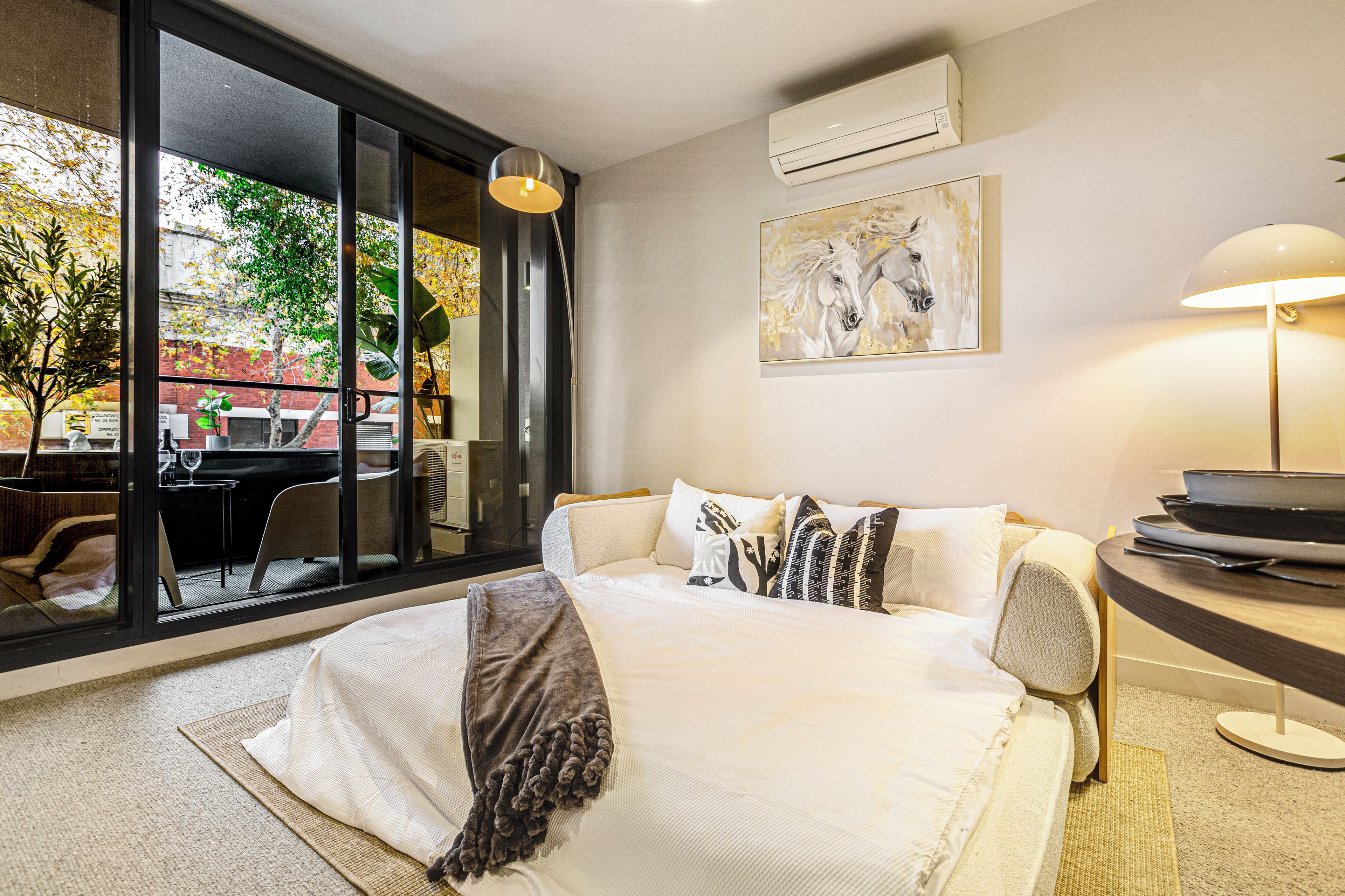 A hotel room with a bed, a desk, a chair, a lamp, and a window with a view of the outside.