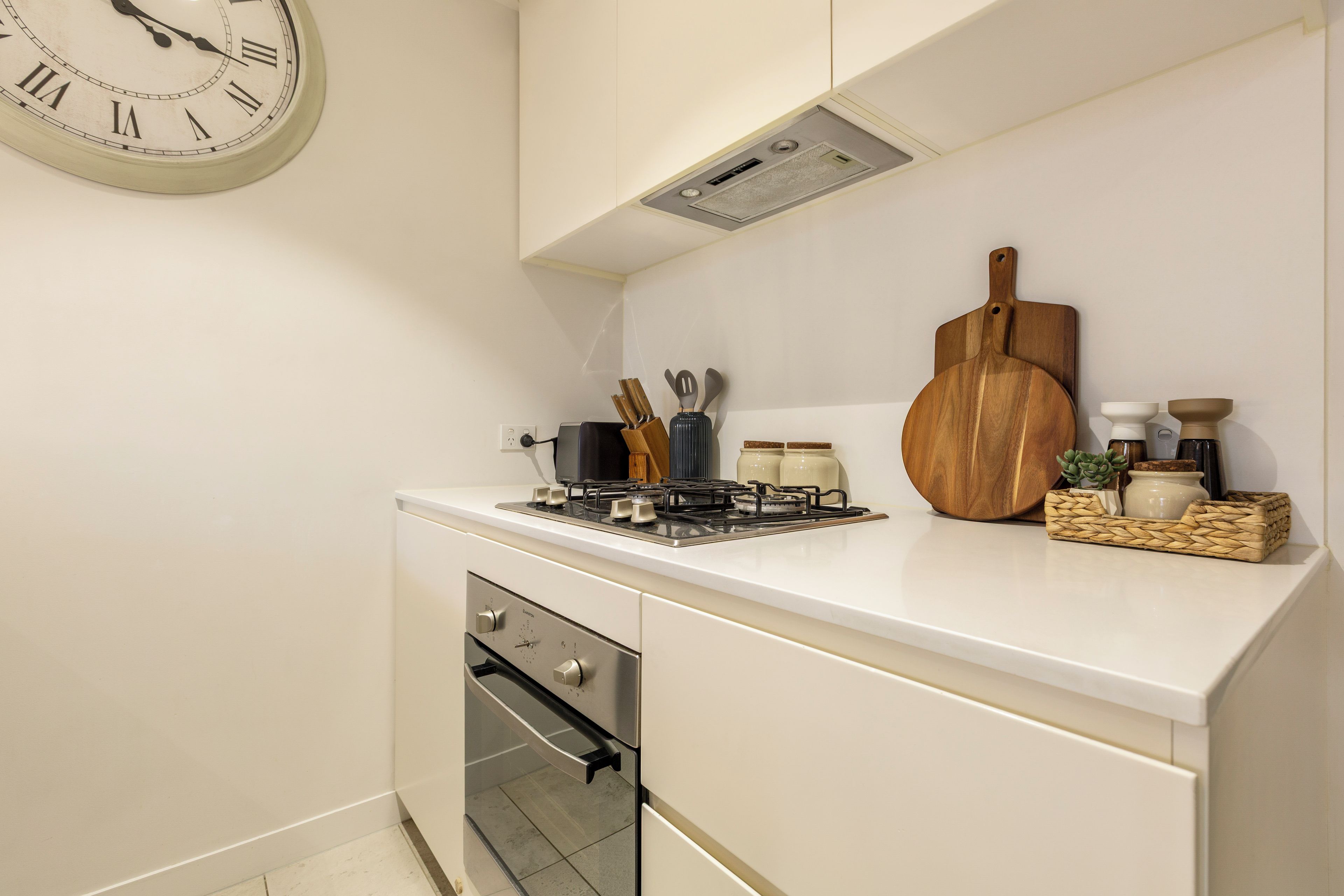 A kitchen with a built-in oven, a stove, and a clock on the wall.