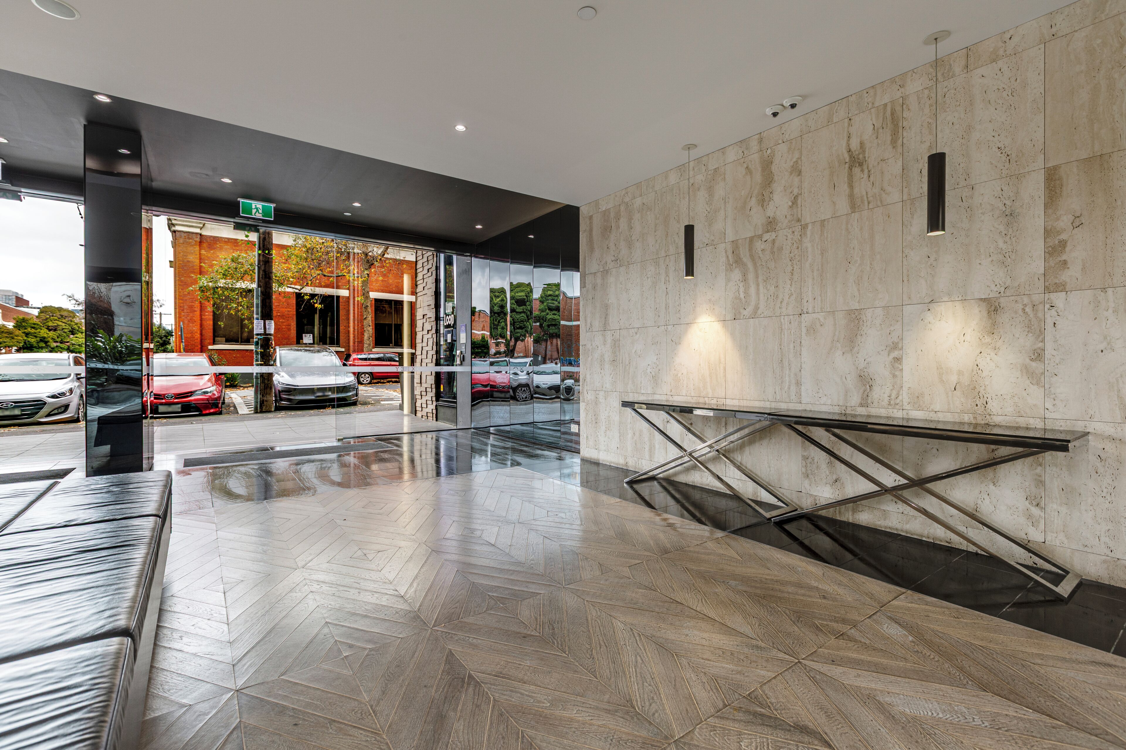 A modern building entrance with a glass facade, a metal staircase, and a parking lot with cars.