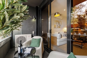 A modern interior with a seating area, a table with a bottle and glass, and a large window with a view of greenery. - Melbourne Escape | Walk to Smith Street | MCG | Free Parking & Balcony (Collingwood)