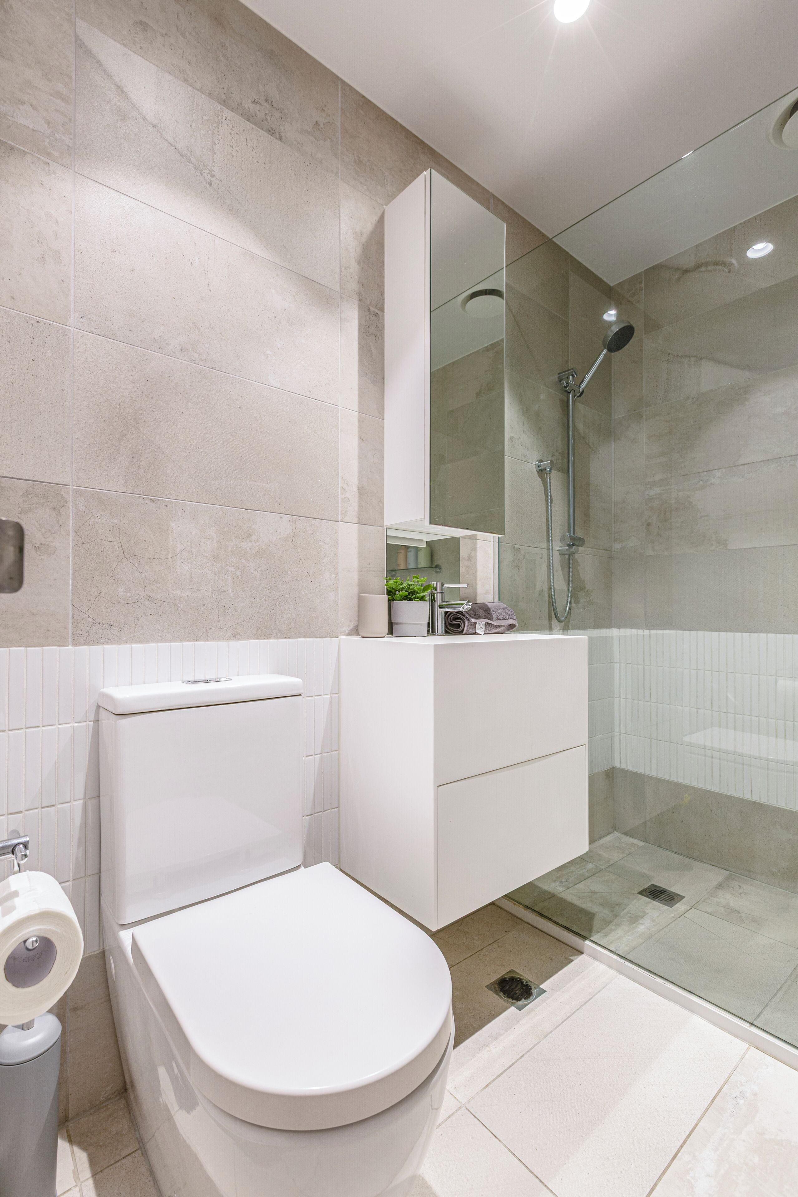 A modern bathroom with a toilet, a glass shower enclosure, and a white vanity.
