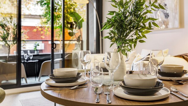 Een eettafel gedekt met borden, kommen, bestek en glazen, met een potplant in het midden.