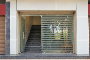 Entrada de un edificio moderno con puerta de vidrio, escaleras que conducen al interior y baranda metálica a la derecha.