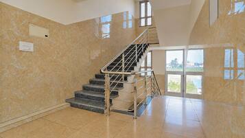 A spacious interior with a marble wall, a staircase with metal railings, and a large window providing a view of the outdoors.