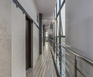 A corridor with a glass railing, a tiled floor, and a door on the left.