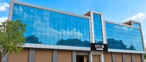 En moderne hotelbygning med en spejlenende glasfacade, et skilt der viser, at det drives af OYO, og et træ i forgrunden.