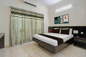 Habitación de hotel con cama, mesita de noche, aire acondicionado instalado en la pared y ventana con cortinas estampadas.